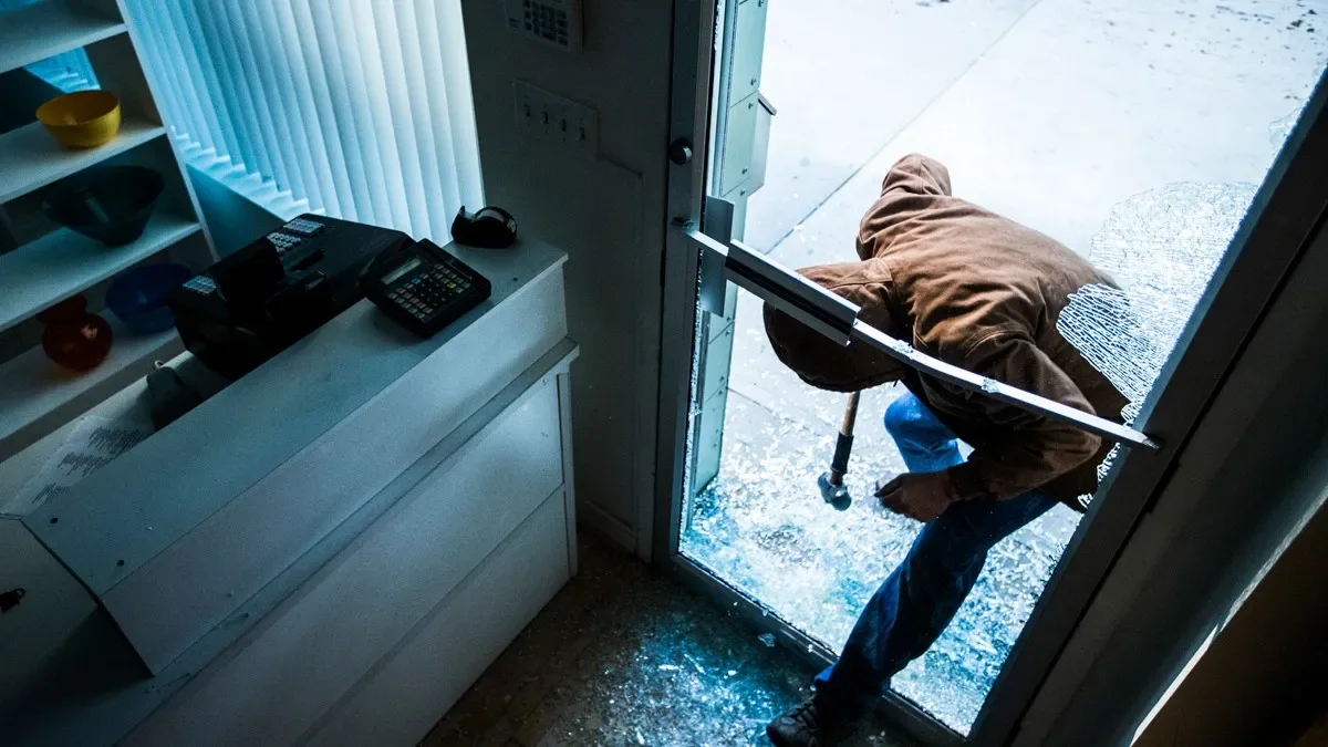 A person entering a home through a broken glass door