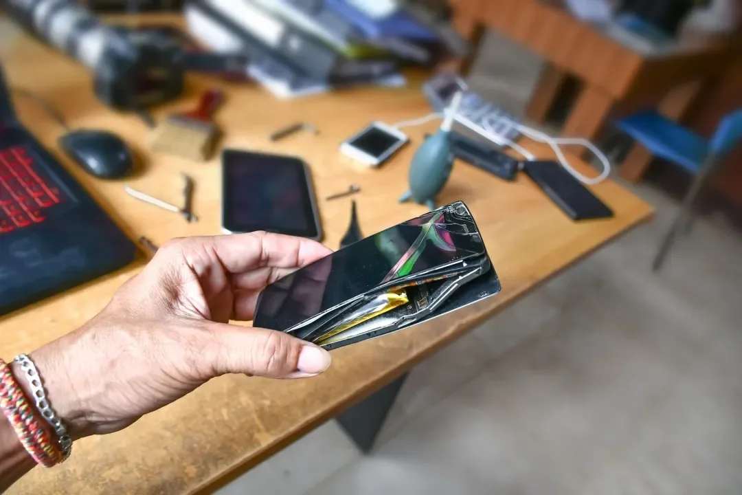 A hand holding a mobile phone with a cracked screen